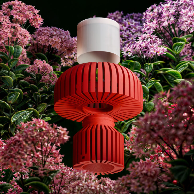A red and white abstract sculpture, reminiscent of a Walmen Dumaliang masterpiece, is surrounded by clusters of pink and purple flowers with lush green leaves