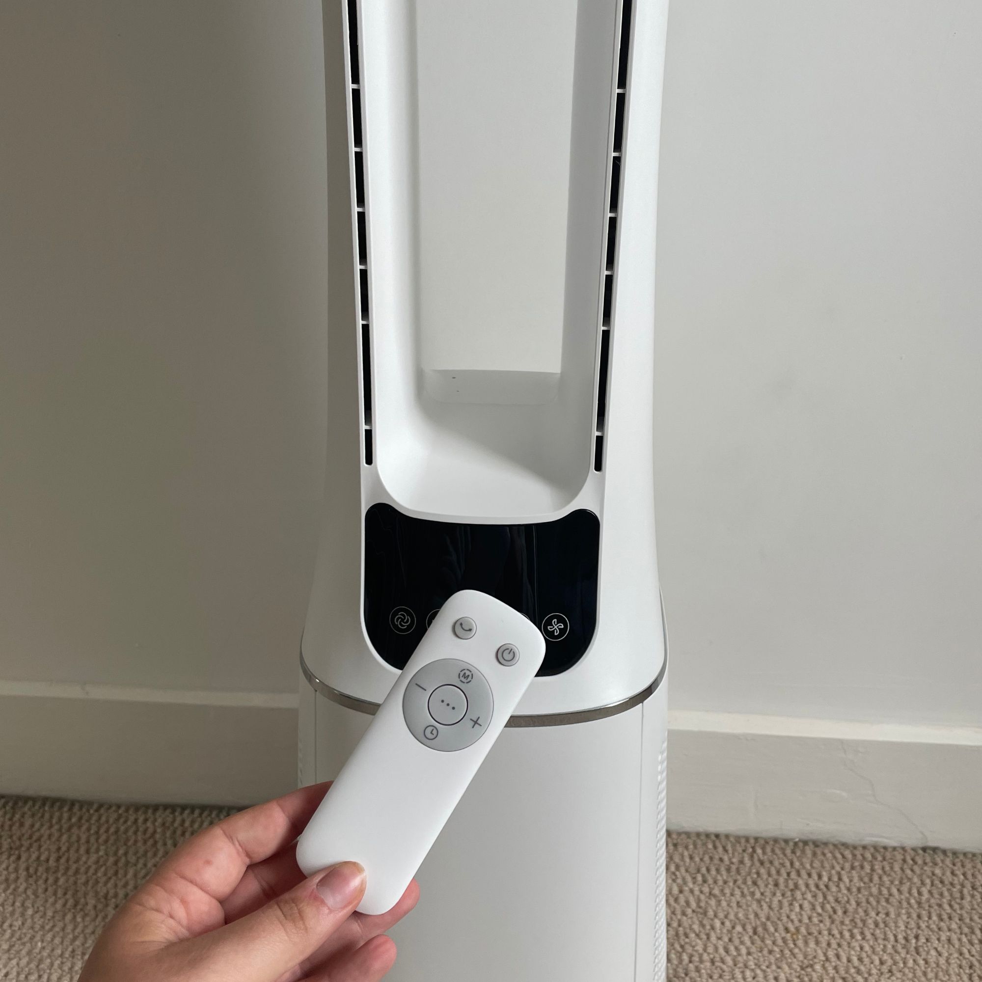 Hand holding the remote in front of the Russell Hobbs RHBLDL12 Bladeless Tower Fan 