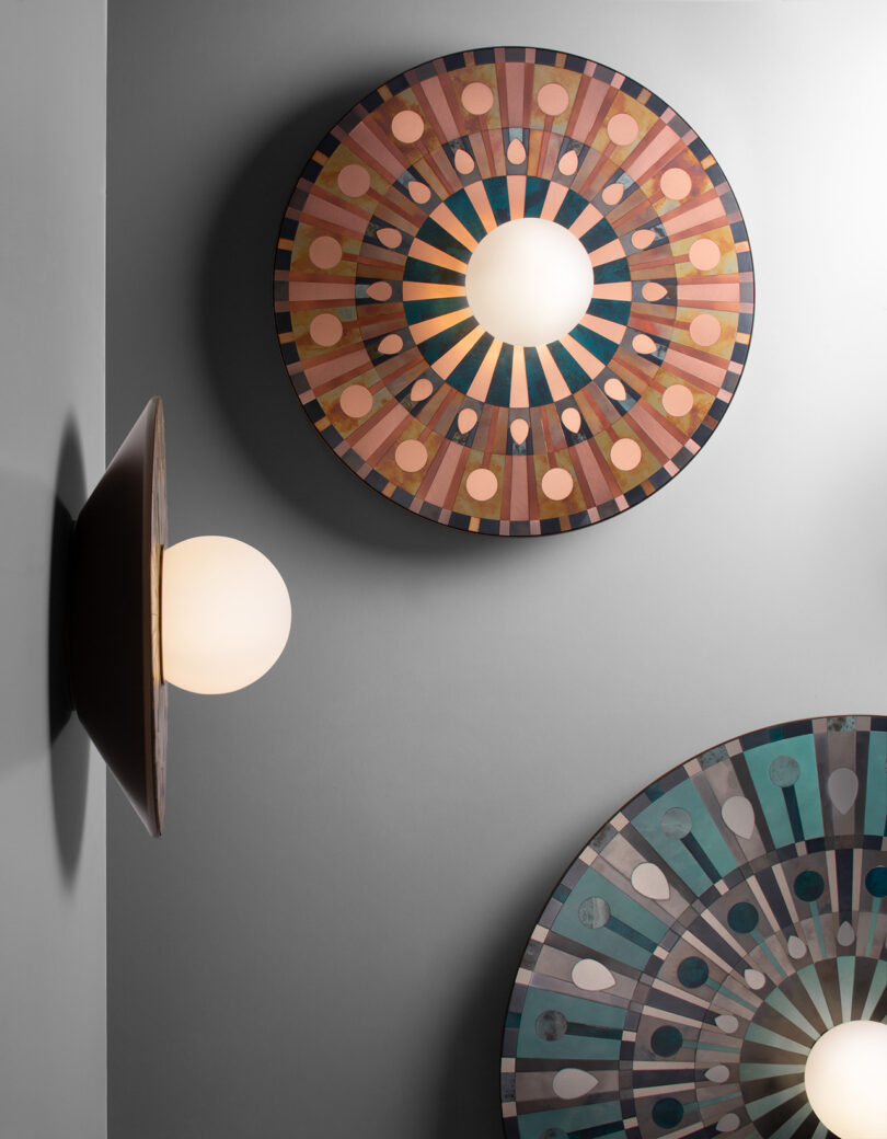 Two circular wall lamps with colorful geometric patterns. The top lamp is brown and blue; the bottom is blue and pink. Each design radiates from a central white light.