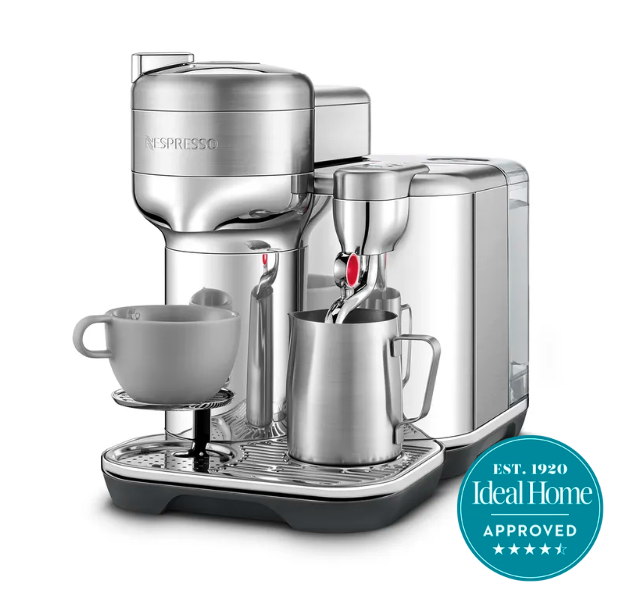 The Nespresso Sage coffee machine with a grey mug lifted up on one side and a milk jug on the other side 