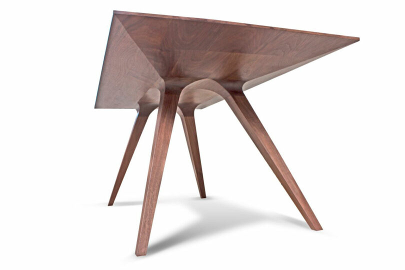 A modern wooden table by Mark Jupiter with four angled legs and a smooth, rectangular top, photographed from a low, side perspective against a white background.