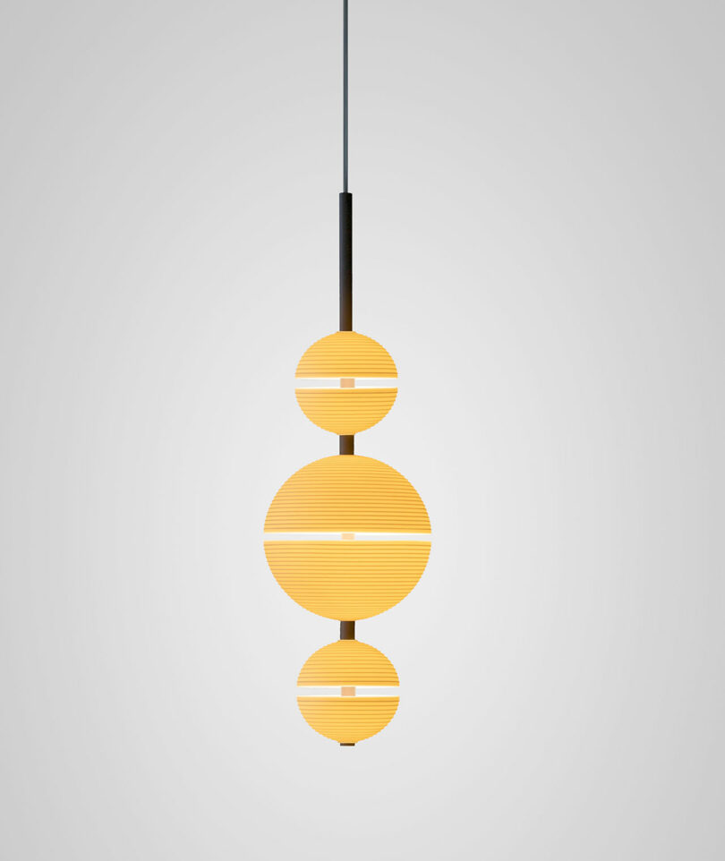 A modern Lee Broom pendant lamp with three stacked, glowing circular sections hangs from a black cord against a plain light gray background.
