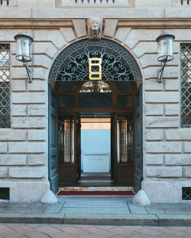 Arched stone entrance with glass doors, metal lanterns, decorative ironwork, and a modern sign reading "HUMAN DESIGN" inside the building.