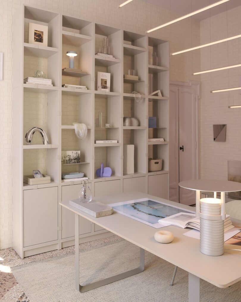 Minimalist office with a large beige shelving unit holding books and decor, a modern desk with papers and objects, and linear ceiling lights