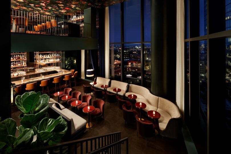 Stylish, dimly lit bar with a modern interior, featuring plush seating, a well-stocked bar, and large windows offering a night view of the city skyline.