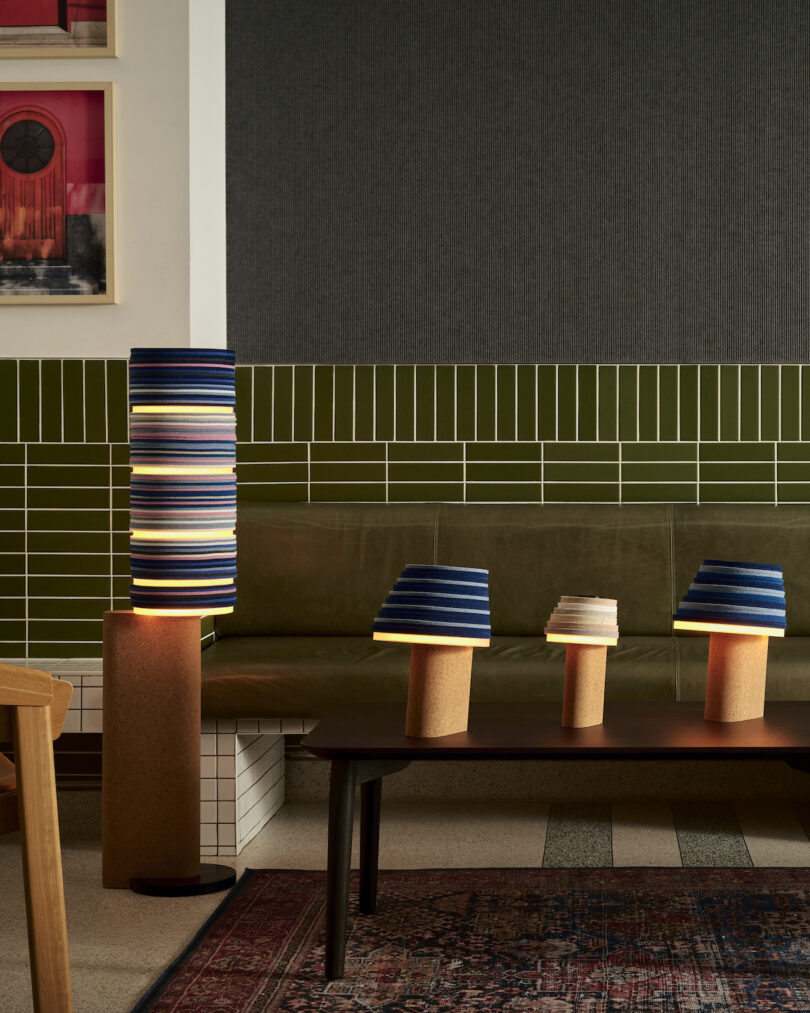 Cozy seating area with green tile and gray walls. Felt and cork lamps with blue and striped shades. Wooden chairs and a patterned rug complete the decor.