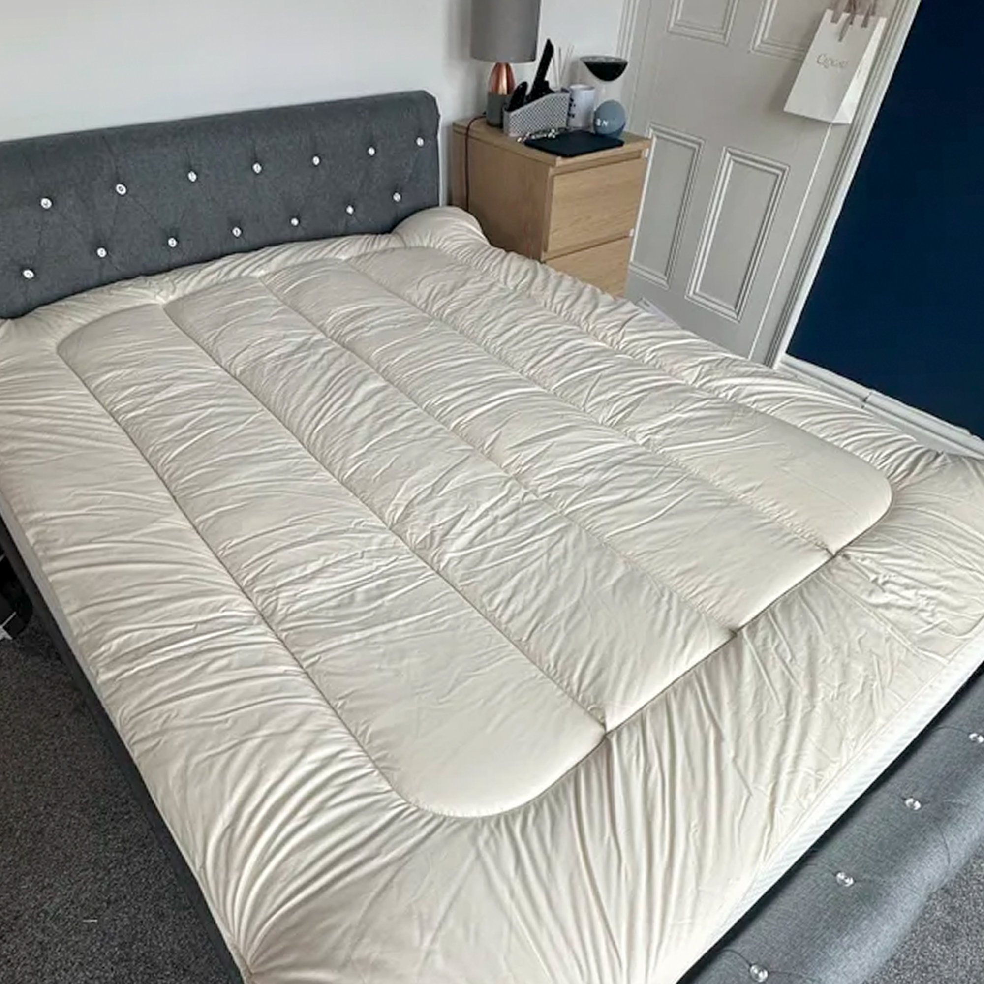 The Woolroom Deluxe Wool Mattress Topper being tested on a grey upholstered bed in a bedroom