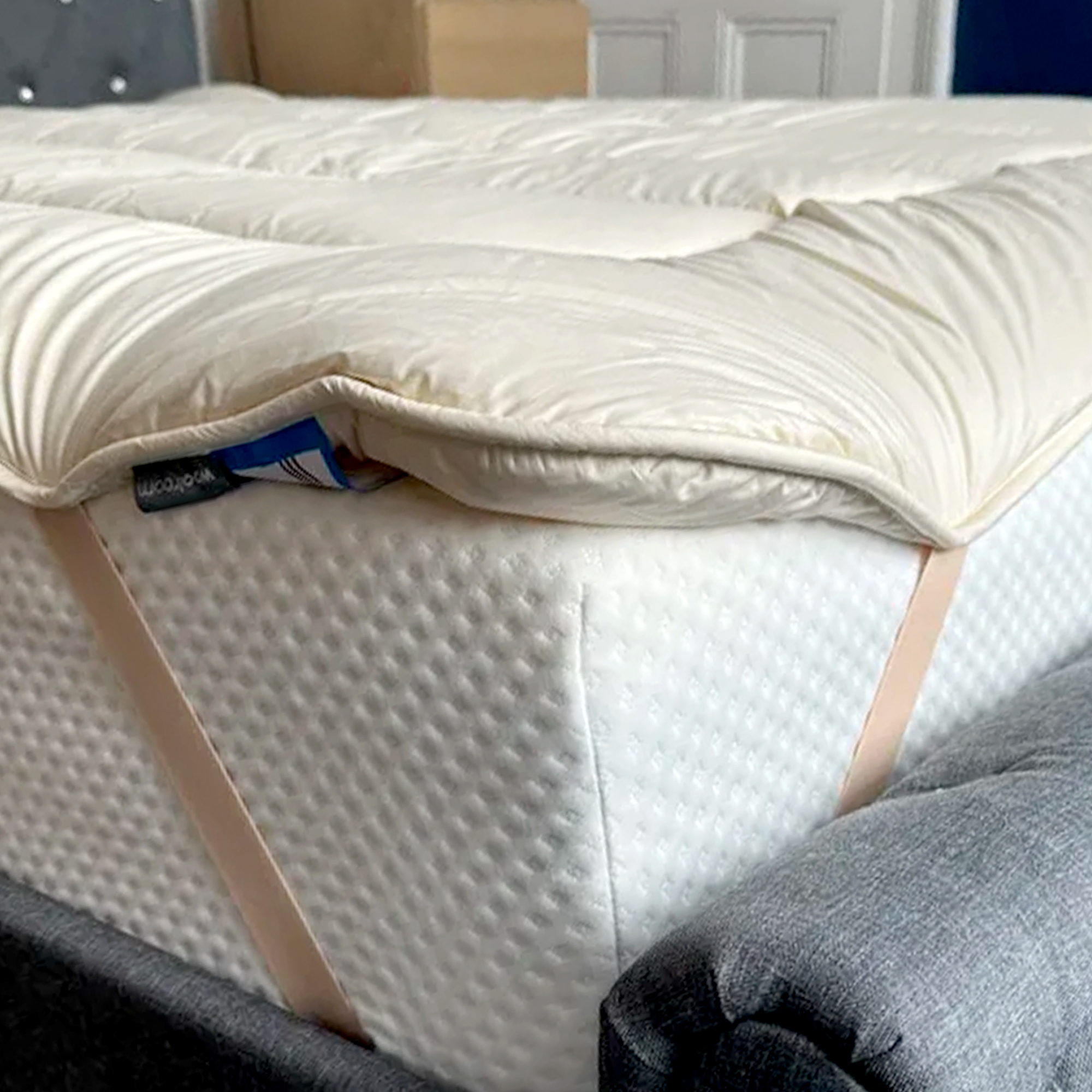 The corner of the  Woolroom Deluxe Wool Mattress Topper showing its elasticated straps holding it in place on a mattress
