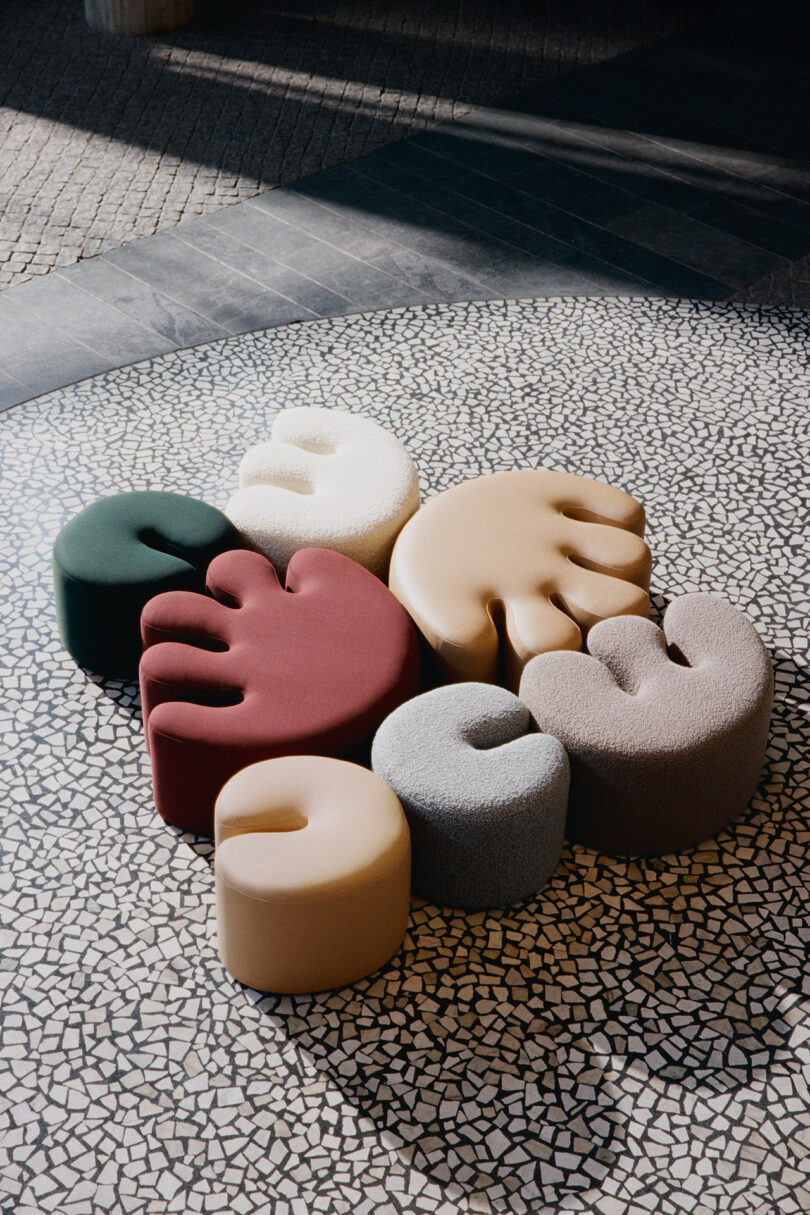 Six colorful, uniquely shaped cushioned seats arranged in a circular pattern on a tiled mosaic floor, viewed from above.