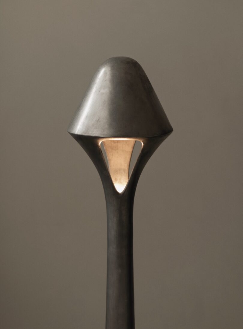 A metallic, abstract lamp with a conical top and a triangular cutout revealing a gold interior, set against a plain background.